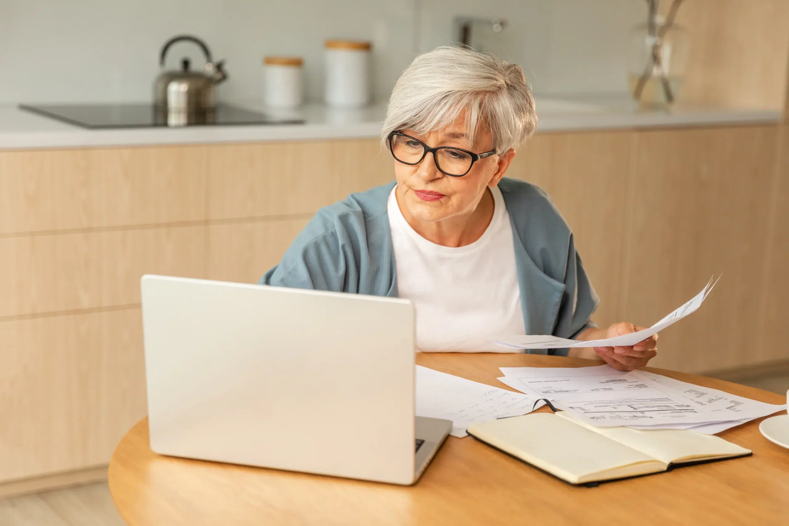Une femme proche de la retraite calcule sa pension de base avec une calculatrice à la table de sa cuisine.