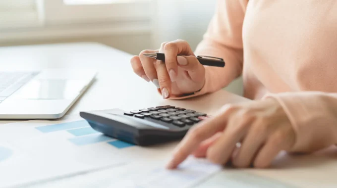 Femme Retraitée Assise à Une Table, Utilisant Une Calculatrice Pour Estimer Le Montant Net De Sa Pension