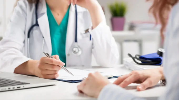 Médecin Libéral âgé En Blouse Blanche En Consultation Avec Un Patient Dans Son Cabinet, Dans Le Cadre D’un Cumul Emploi-retraite.