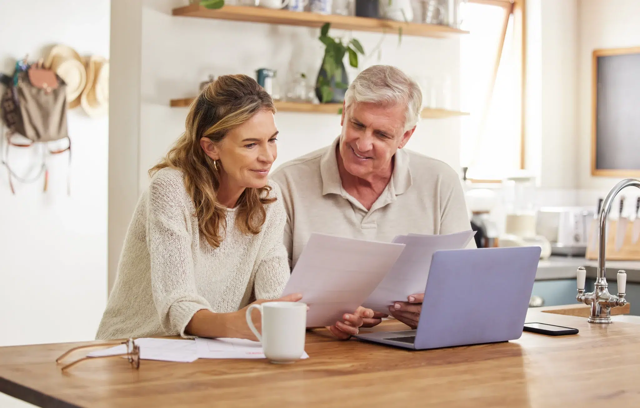 Couple d’entrepreneurs travaillant sur la retraite du conjoint collaborateur devant un ordinateur dans leur cuisine