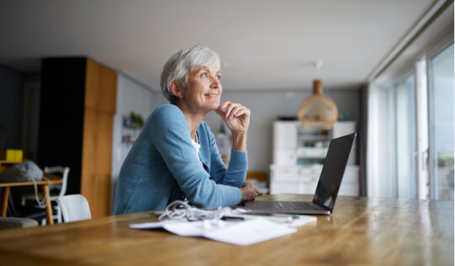 Femme Senior Consultant Ses Droits à La Retraite AGIRC-ARRCO Après Un Arrêt Maladie, Devant Un Ordinateur Portable à Domicile